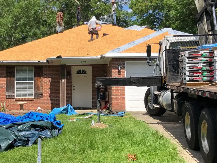 Roofing crew mid tear-off with materials on site
