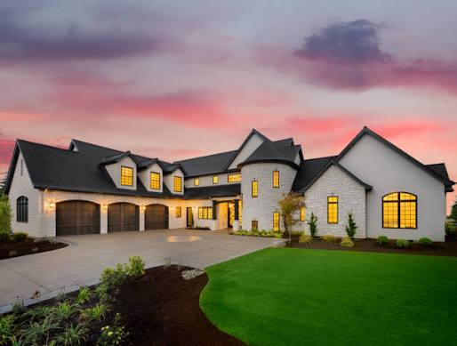 Large home at dusk with lit windows and a finished roof